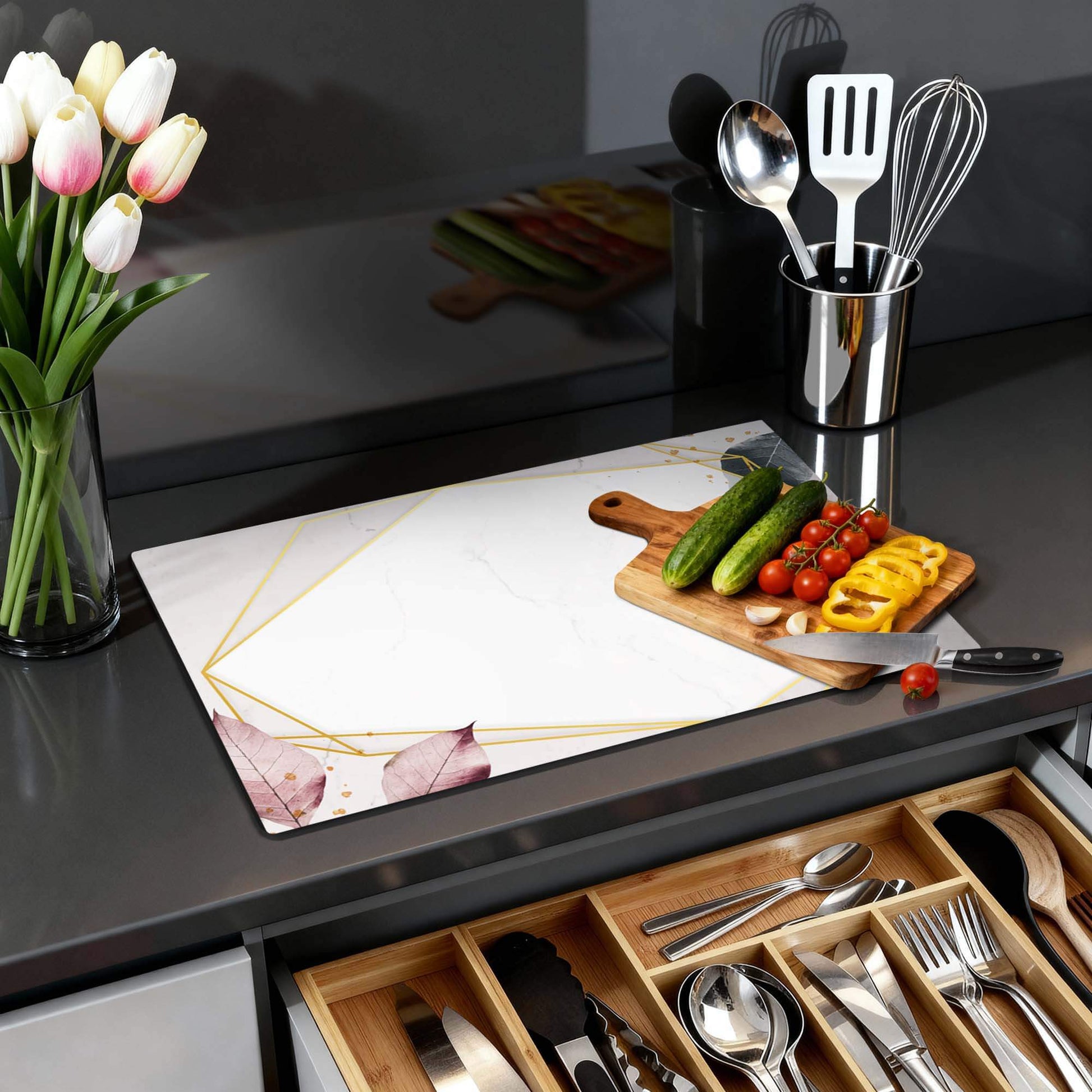 Geometrische Eleganz - Herdabdeckplatte auf einer Arbeitsplatte mit Gemüse und einer Vase mit Tulpen.