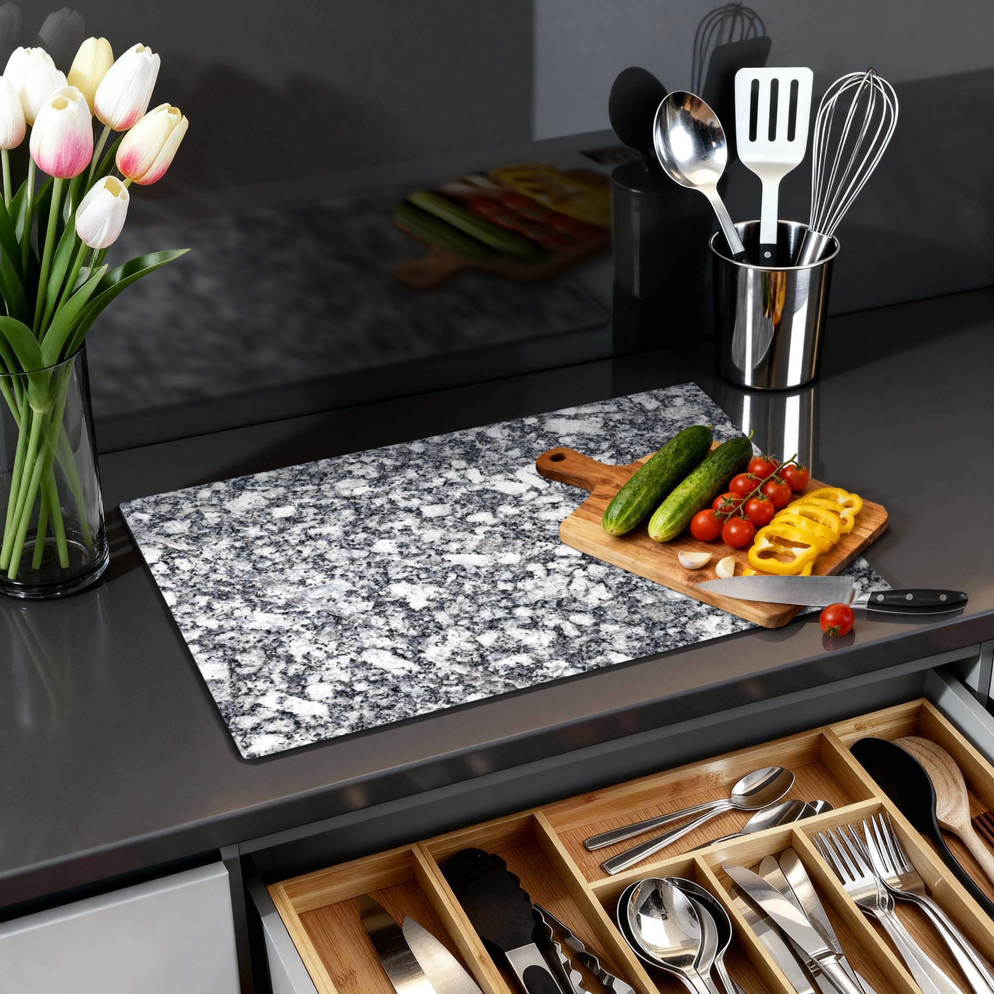 Midnight Granite - Induktionswächter auf einer Küchenplatte mit Gemüse und Blumen im Hintergrund.