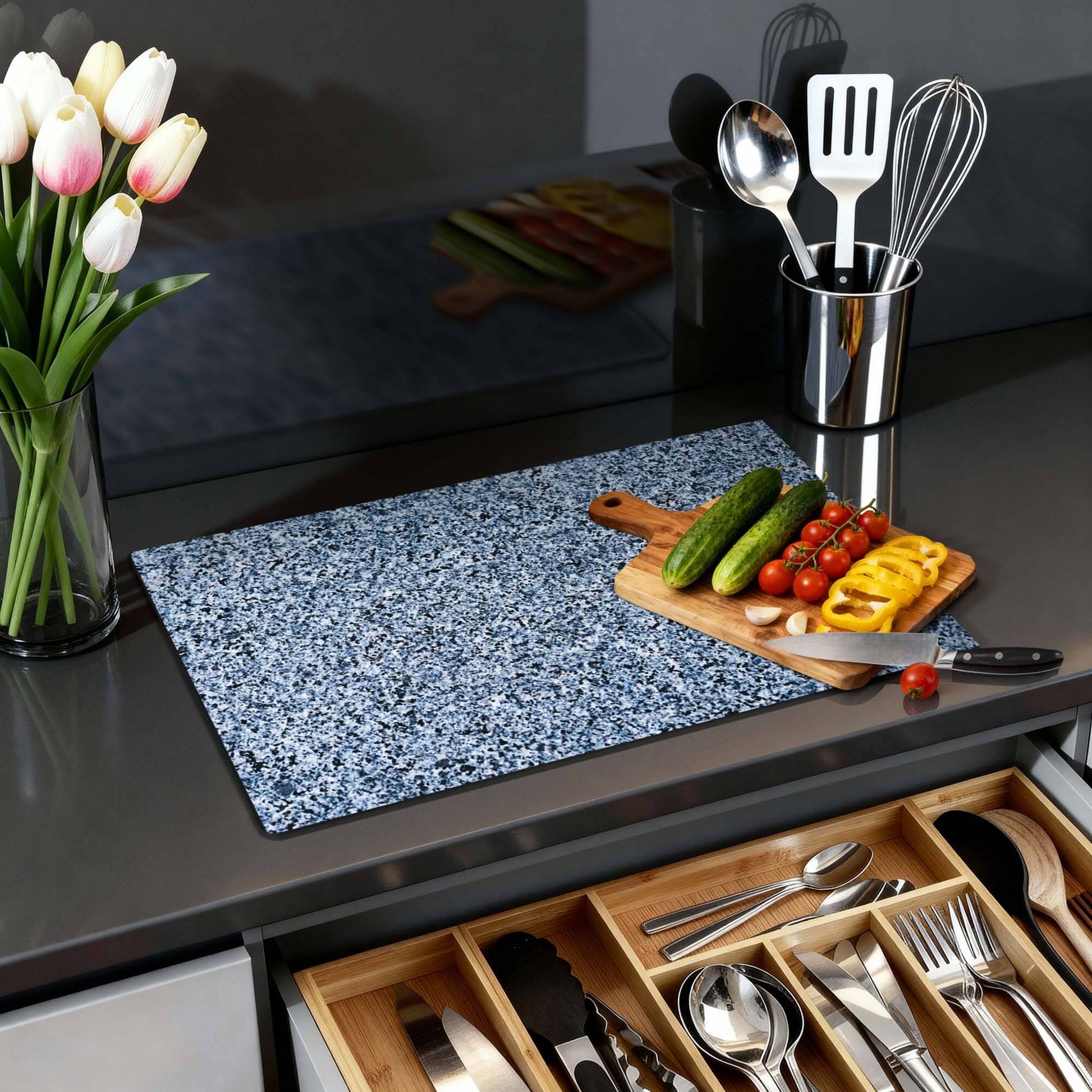 Baltischer Granit - Herdabdeckplatte auf einer Küchenarbeitsplatte mit Gemüse, Schneidebrett und Blumen.