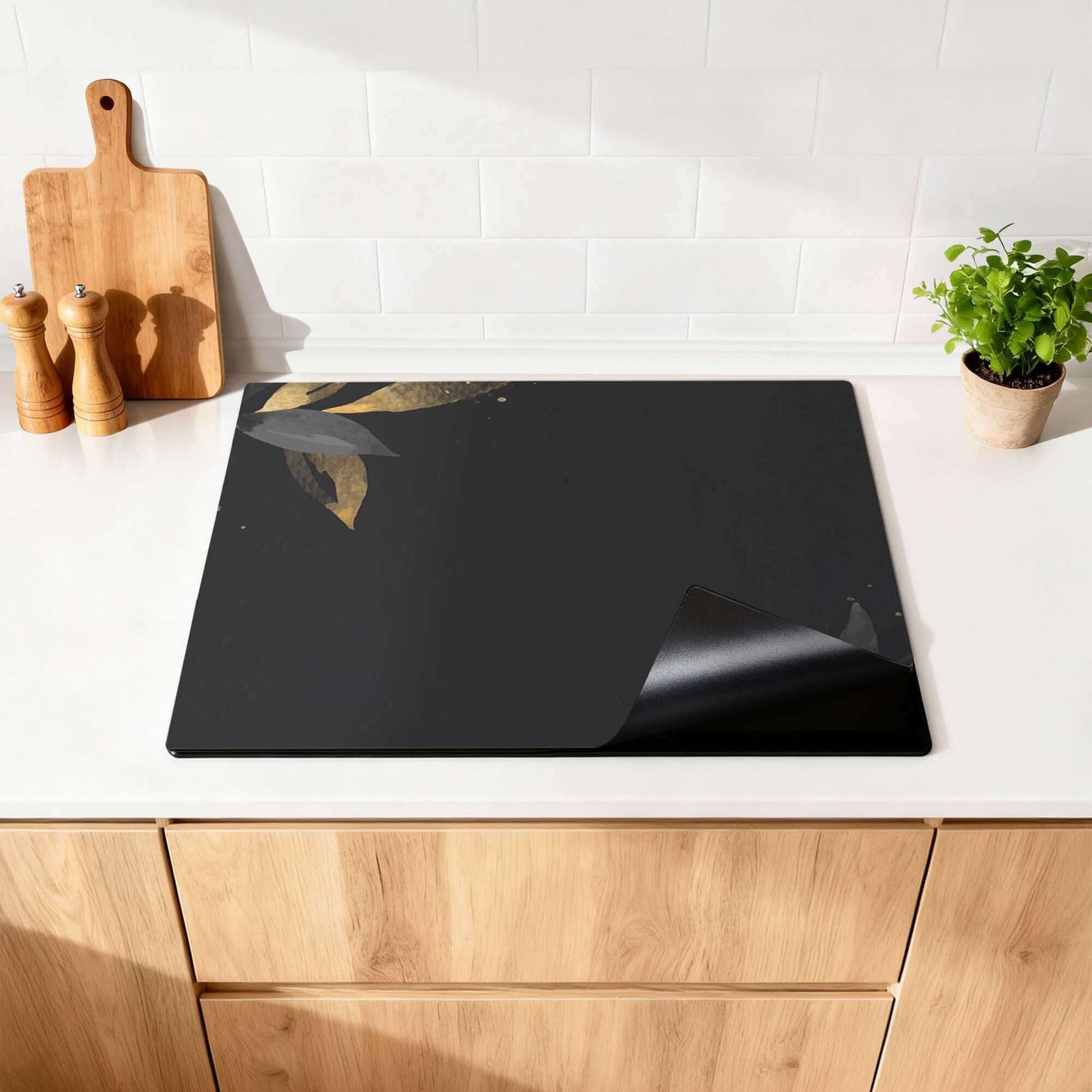 Black Olive - Herdabdeckplatte auf einer modernen Küchenarbeitsplatte mit stilvollen goldenen Olivenblättern.