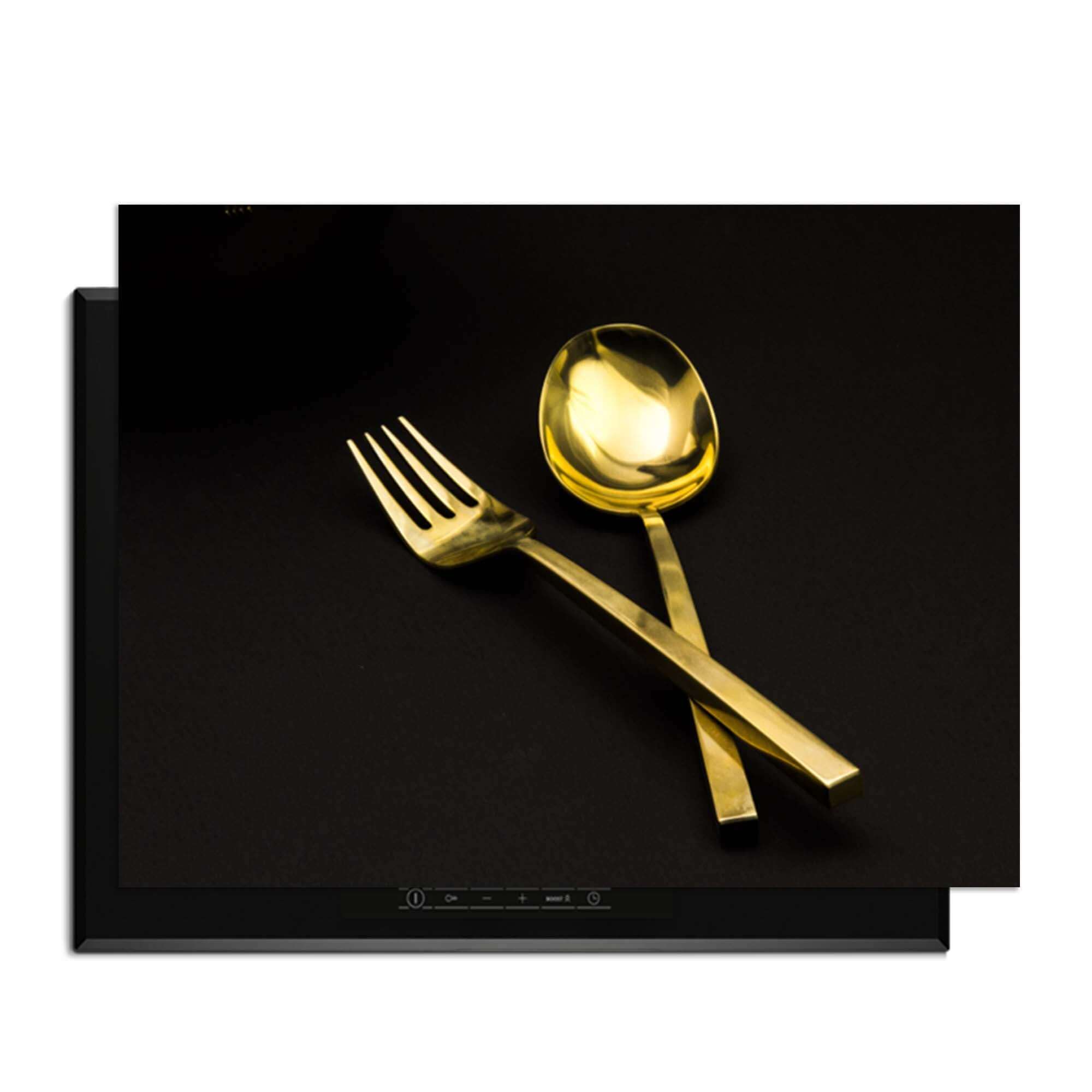 Dining Deluxe - Herdabdeckplatte mit goldenem Besteck auf schwarzem Hintergrund.