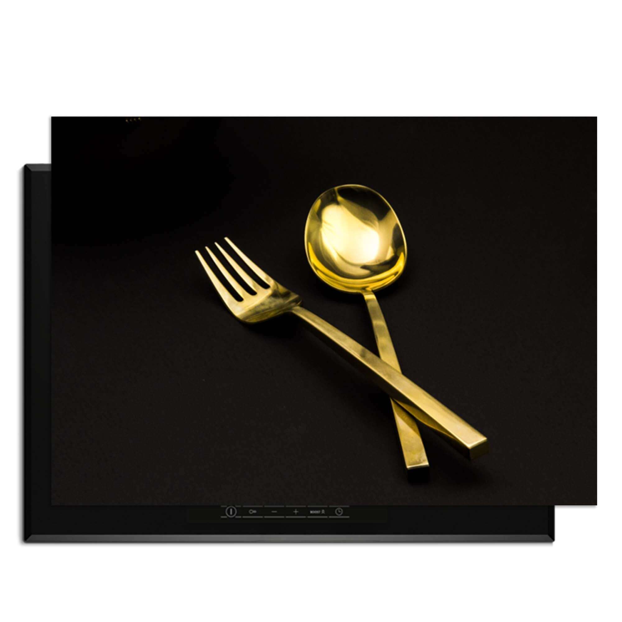 Dining Deluxe - Herdabdeckplatte mit goldenem Besteck auf schwarzem Hintergrund.