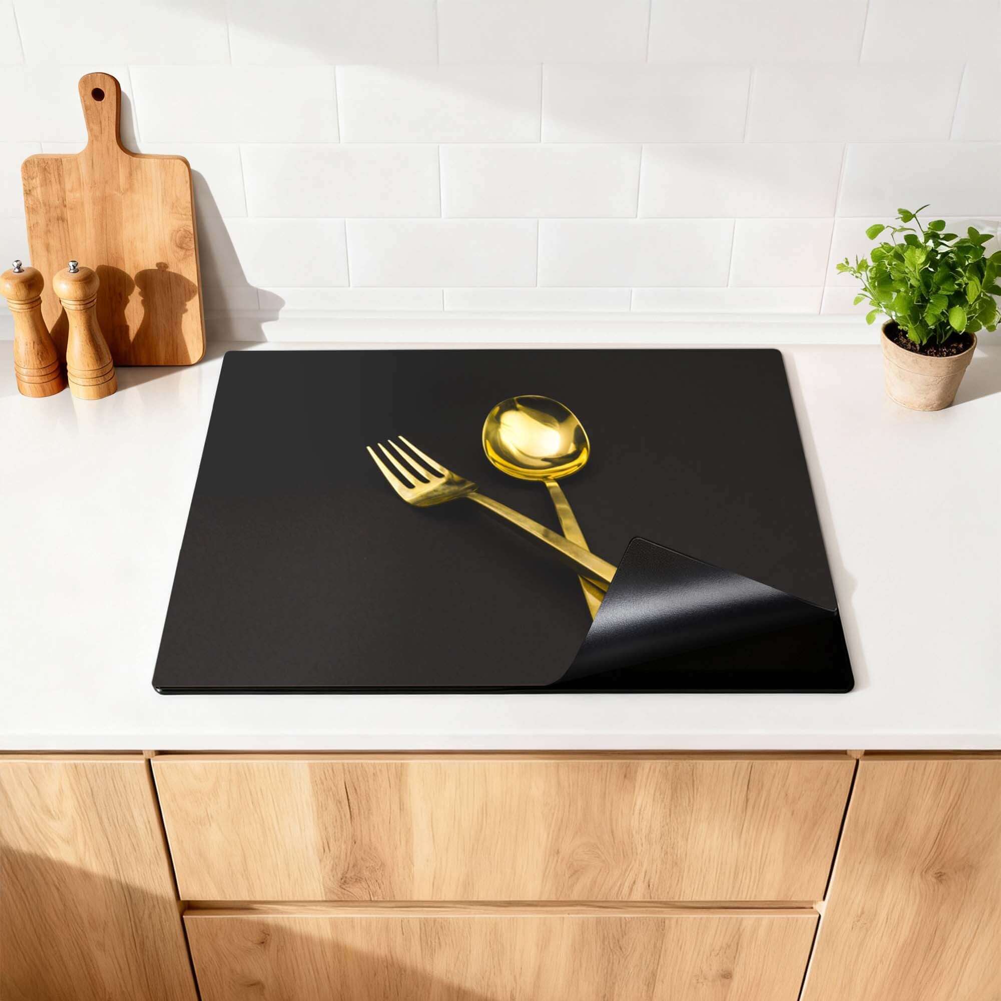 Dining Deluxe - Herdabdeckplatte mit goldener Gabel und Löffel auf schwarzem Hintergrund.